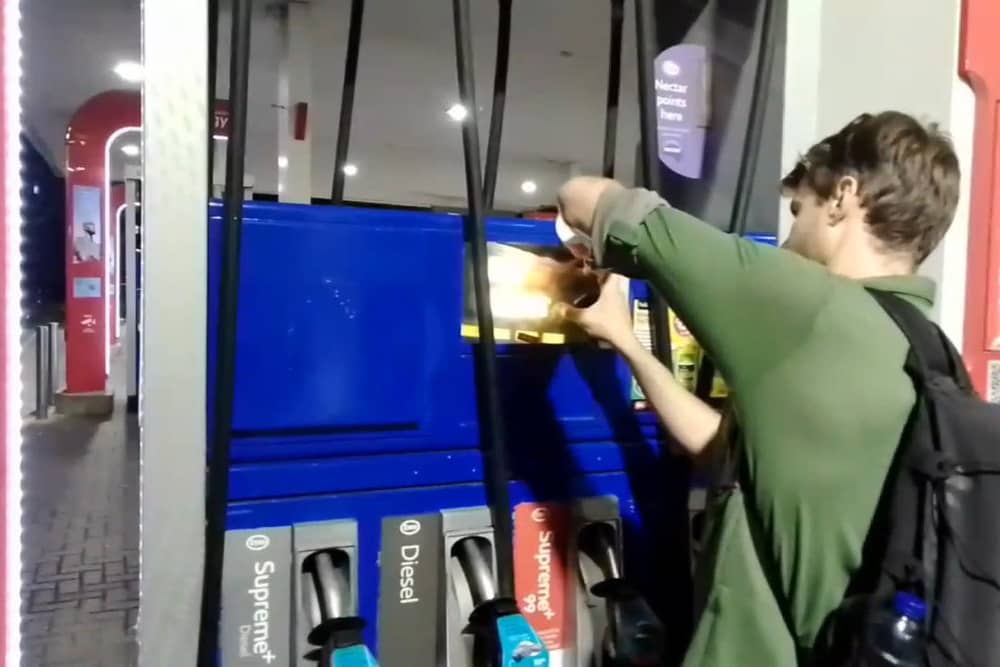 Dr Patrick Hart cracks the display panels of petrol pumps at Esso Thurrock Services on the M25 on August 24 2022. 
