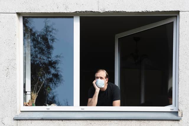 A man wearing a face mask looks out of his flat window. Photo: Shutterstock