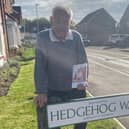 Bertnext to Hedgehog Way, holding a copy of his book.