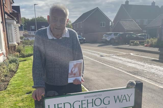 Bertnext to Hedgehog Way, holding a copy of his book.