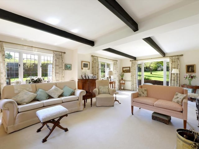 The character sitting room has a lovely fireplace, feature ceiling beams and windows to three walls with doors leading out to the gardens.