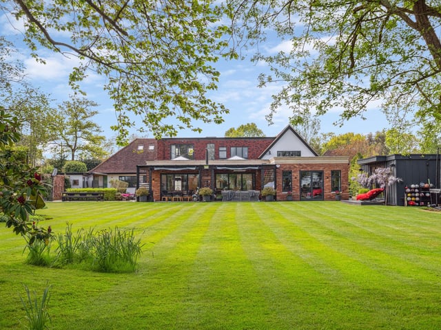 A rea view of the house with gardens mainly laid to lawn , mature trees and further seating areas located throughout the grounds.
