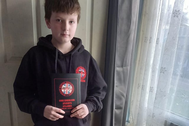 12-year-old Ryan represents his kickboxing class, U.M A.I Kickboxing,  as he stands with its syllabus
