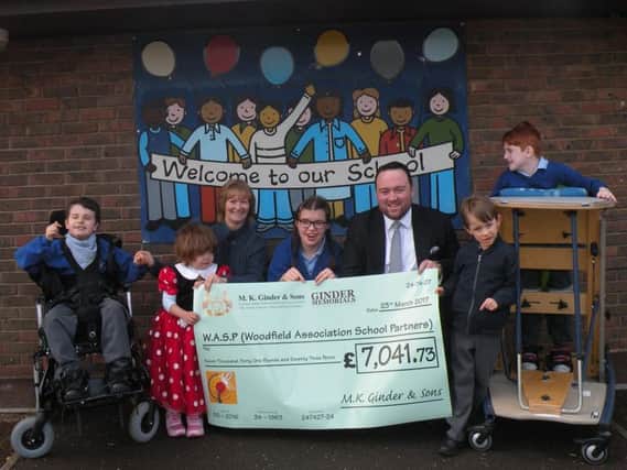 Adam Ginder presents the cheque to Woodfield's deputy head teacher Beverley Hamilton as students look on